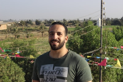 Man with beard wearing casual shirt smiling warmly in outdoor setting with soft lighting